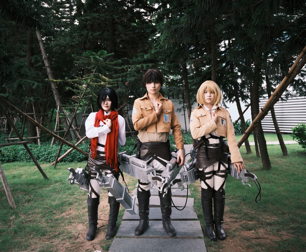 three cosplayers in detailed anime costumes pose outdoors amidst trees