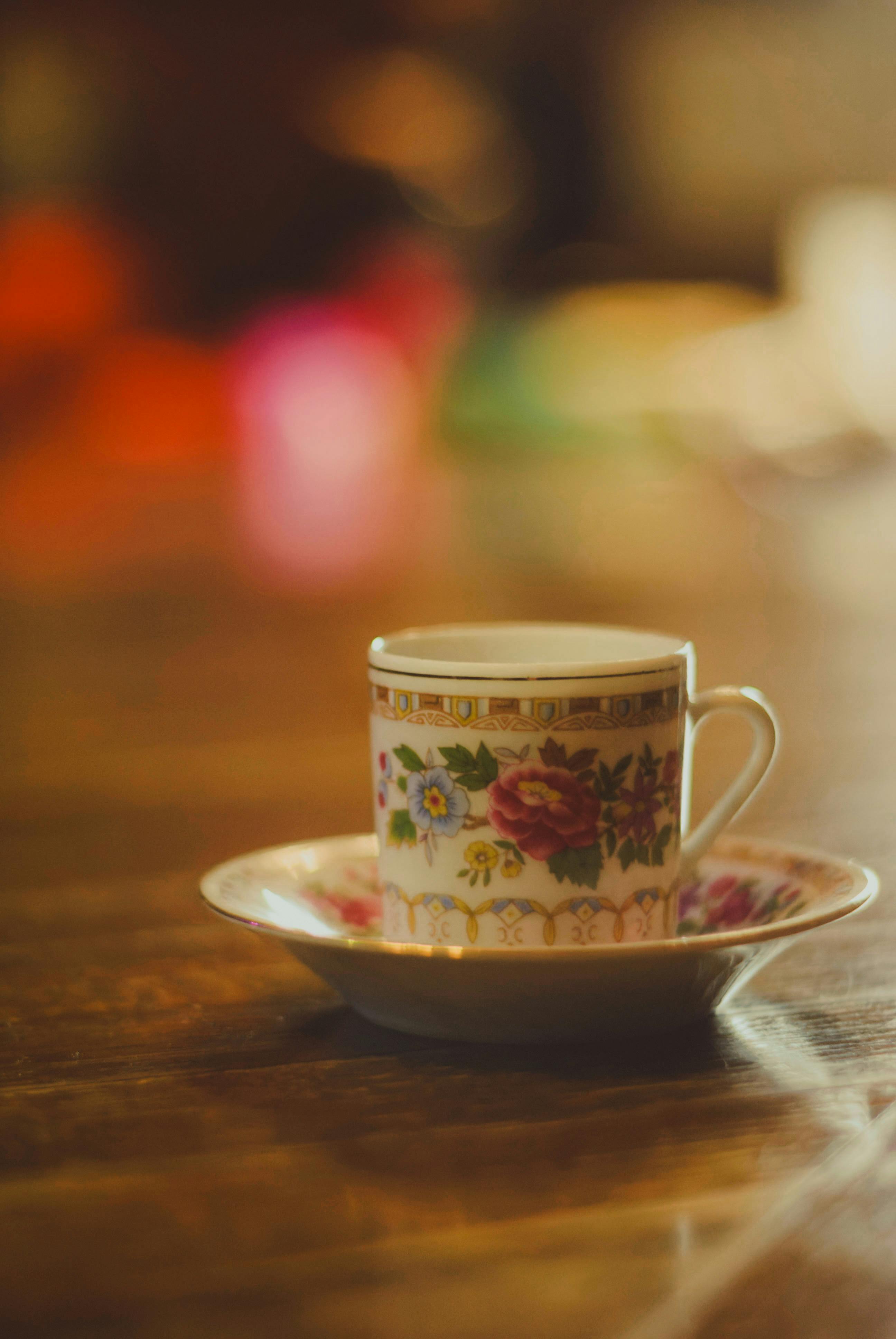 A beautifully decorated vintage teacup with floral motifs sits on a wooden table, exuding a warm, nostalgic atmosphere.