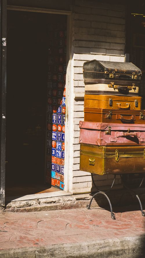 Free A stack of vintage suitcases outside a shop with decorative tiles, capturing an antique vibe. Stock Photo