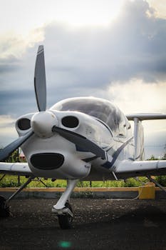 A compact single-engine aircraft stands ready on the runway beneath cloudy skies, perfect for aviation enthusiasts.
