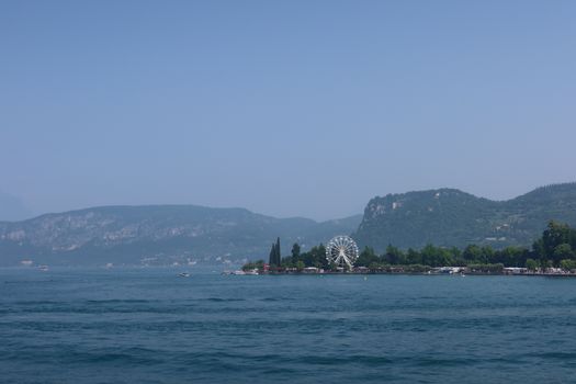 Serene landscape of Lake Garda featuring a distant Ferris wheel and lush greenery.