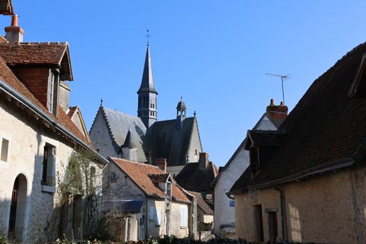 Quaint medieval village scene featuring traditional French architecture and a prominent church steeple under a clear blue sky.