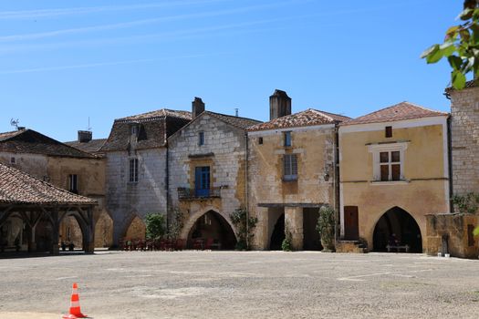 Historic medieval buildings in a quiet French village under a clear blue sky.