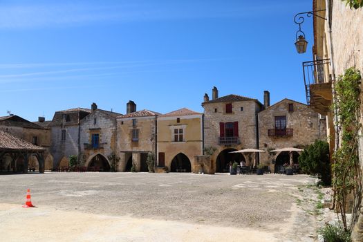 Quaint medieval buildings surround a peaceful village square under a bright blue sky.