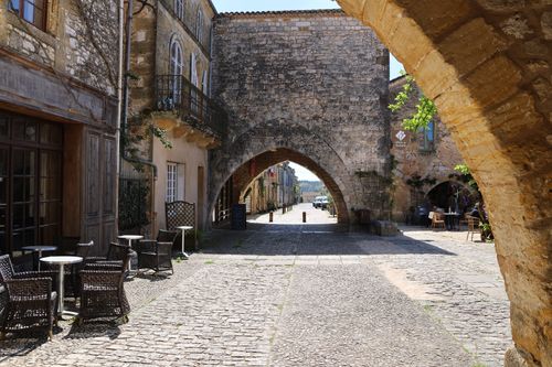 Free Quiet medieval street scene with stone archway and wicker furniture under sunlight. Stock Photo