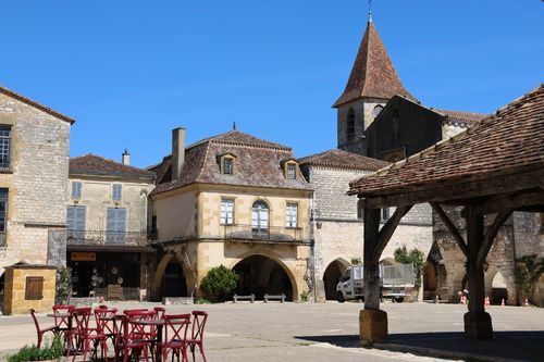 Free A picturesque French village square with rustic architecture and empty outdoor seating on a sunny day. Stock Photo