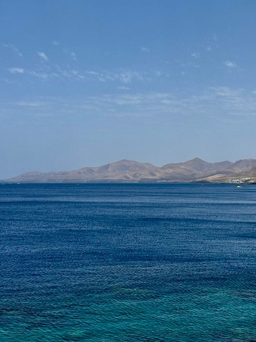Free Beautiful view of Lanzarote coastline with clear blue ocean and distant mountains under a blue sky. Stock Photo