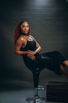Striking portrait of woman in black dress sitting stylishly on a modern chair.
