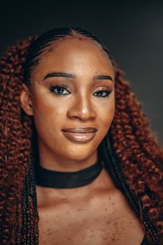 Close-up of a woman with braided hair and natural makeup, smiling confidently.