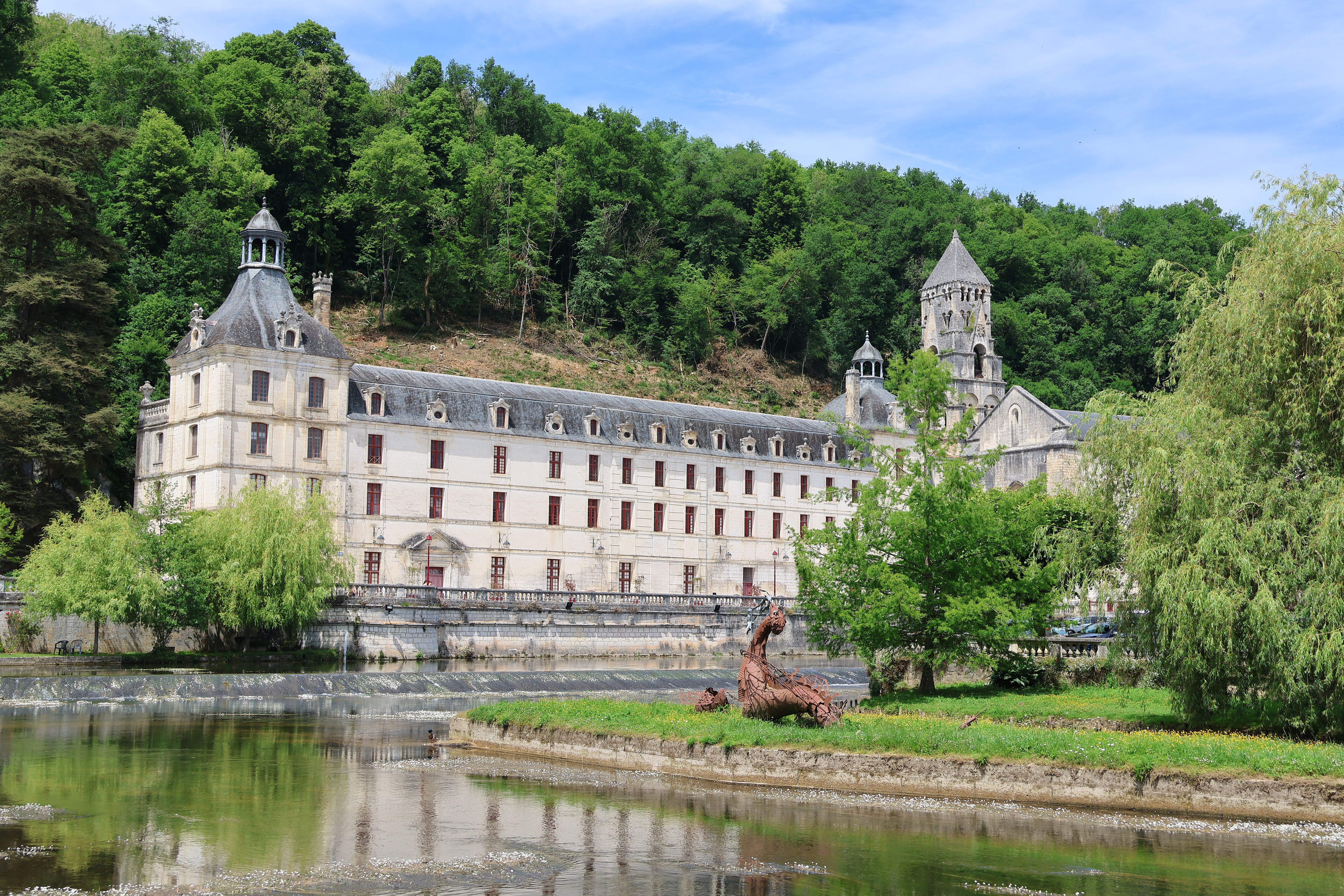 Historic abbey nestled in lush greenery under a clear blue sky, reflecting in tranquil waters.