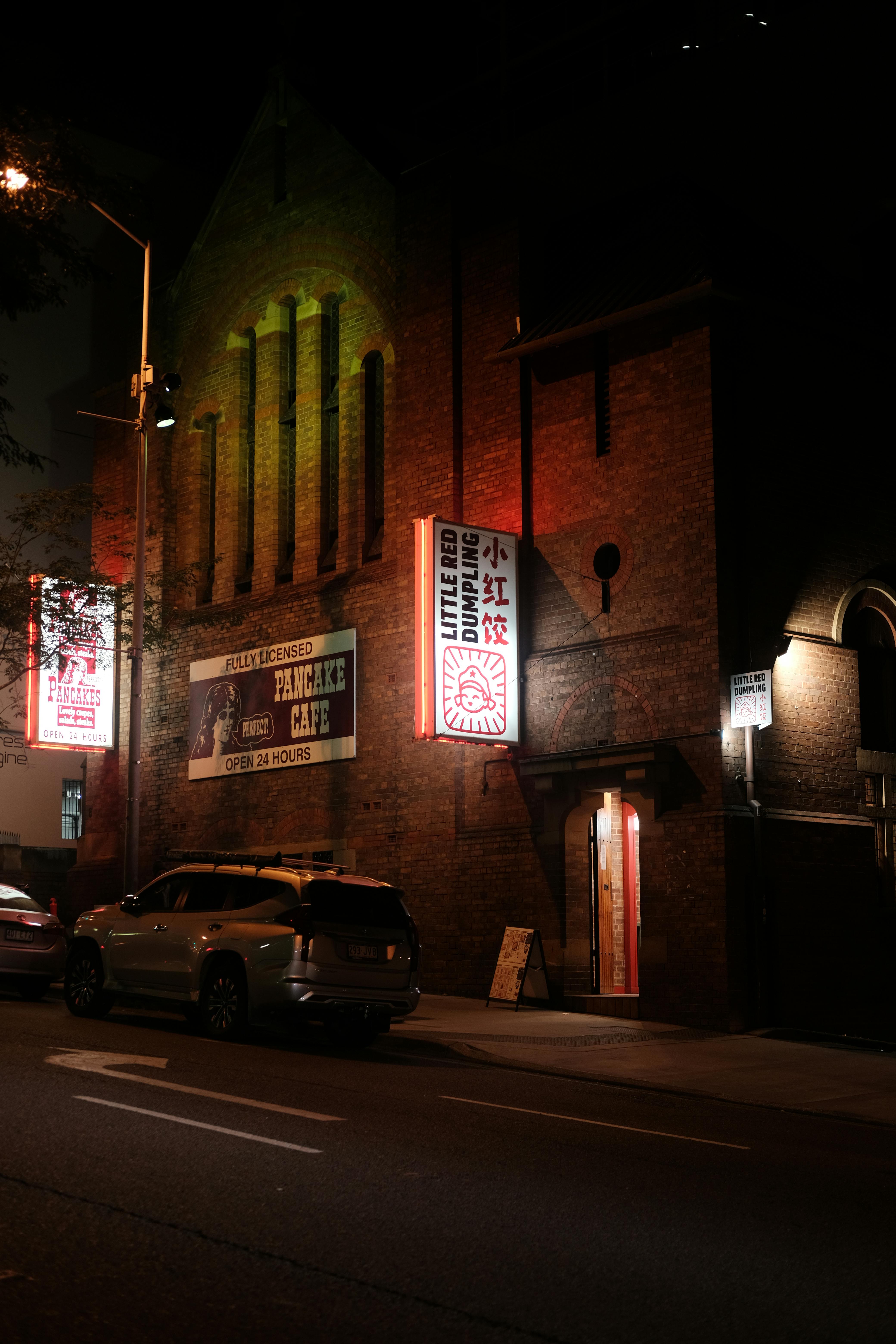 Ücretsiz Sessiz bir sokakta neon tabelalarla aydınlatılmış, aydınlık bir şehir kafesinin yer aldığı gece manzarası. Stok Fotoğraflar