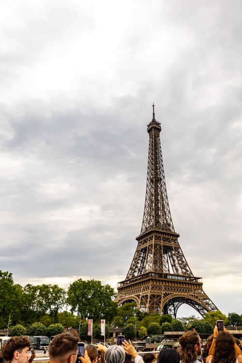 Free Scenic view of the Eiffel Tower in Paris with tourists capturing the moment under an overcast sky. Stock Photo