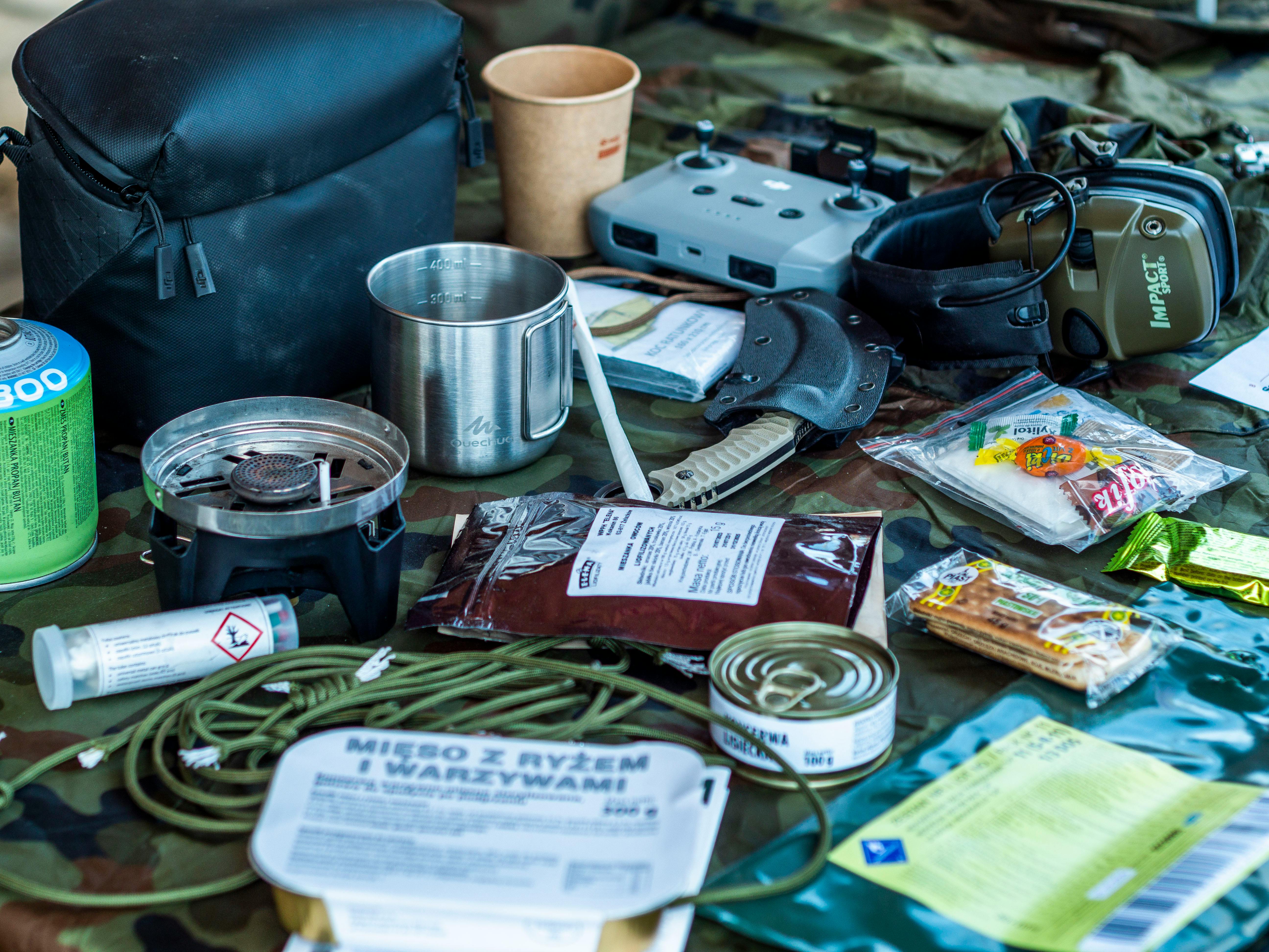 A diverse assortment of camping and survival items laid out, including food, tools, and gadgets.