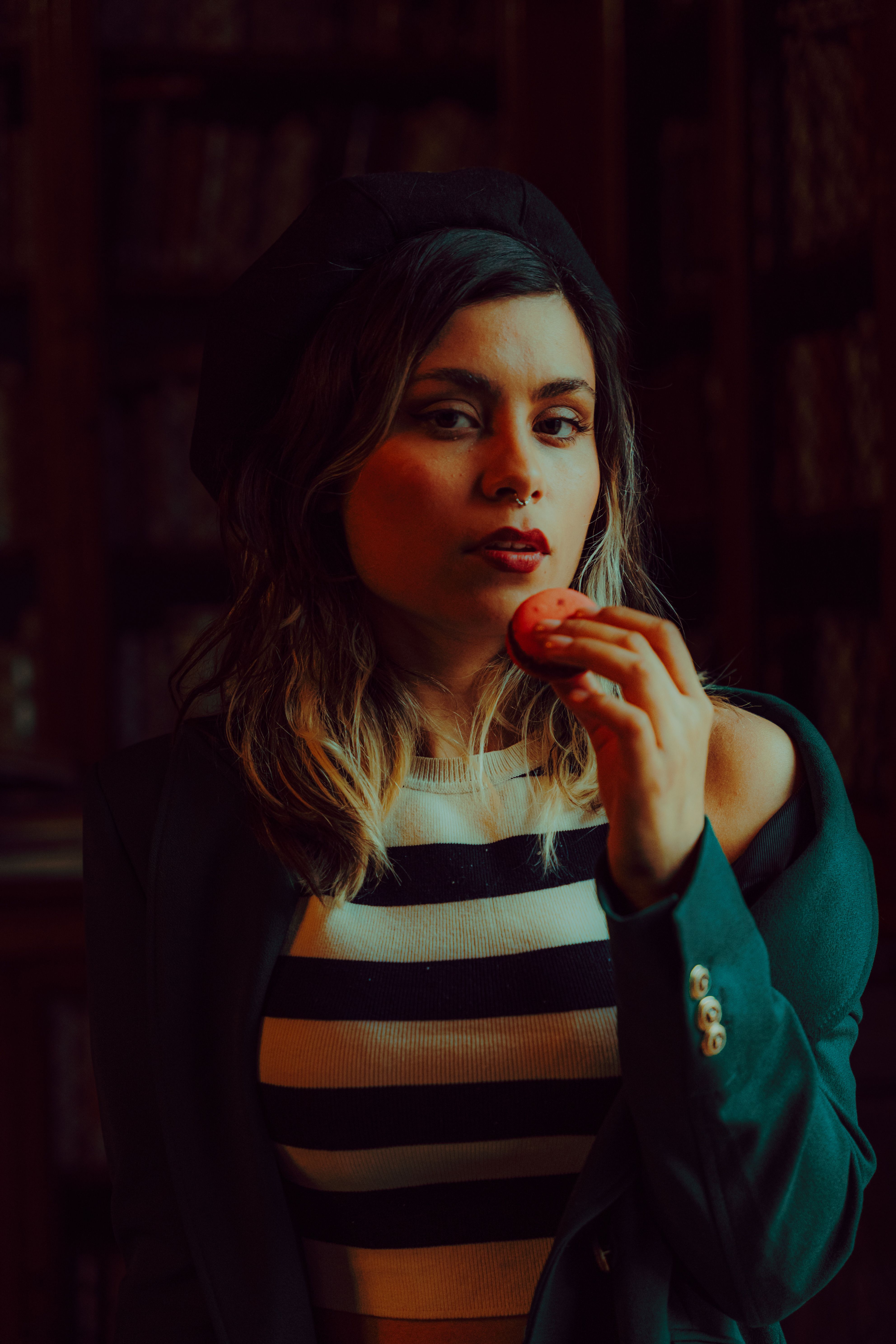 Stylish woman in chic attire holding a macaron in an indoor setting.