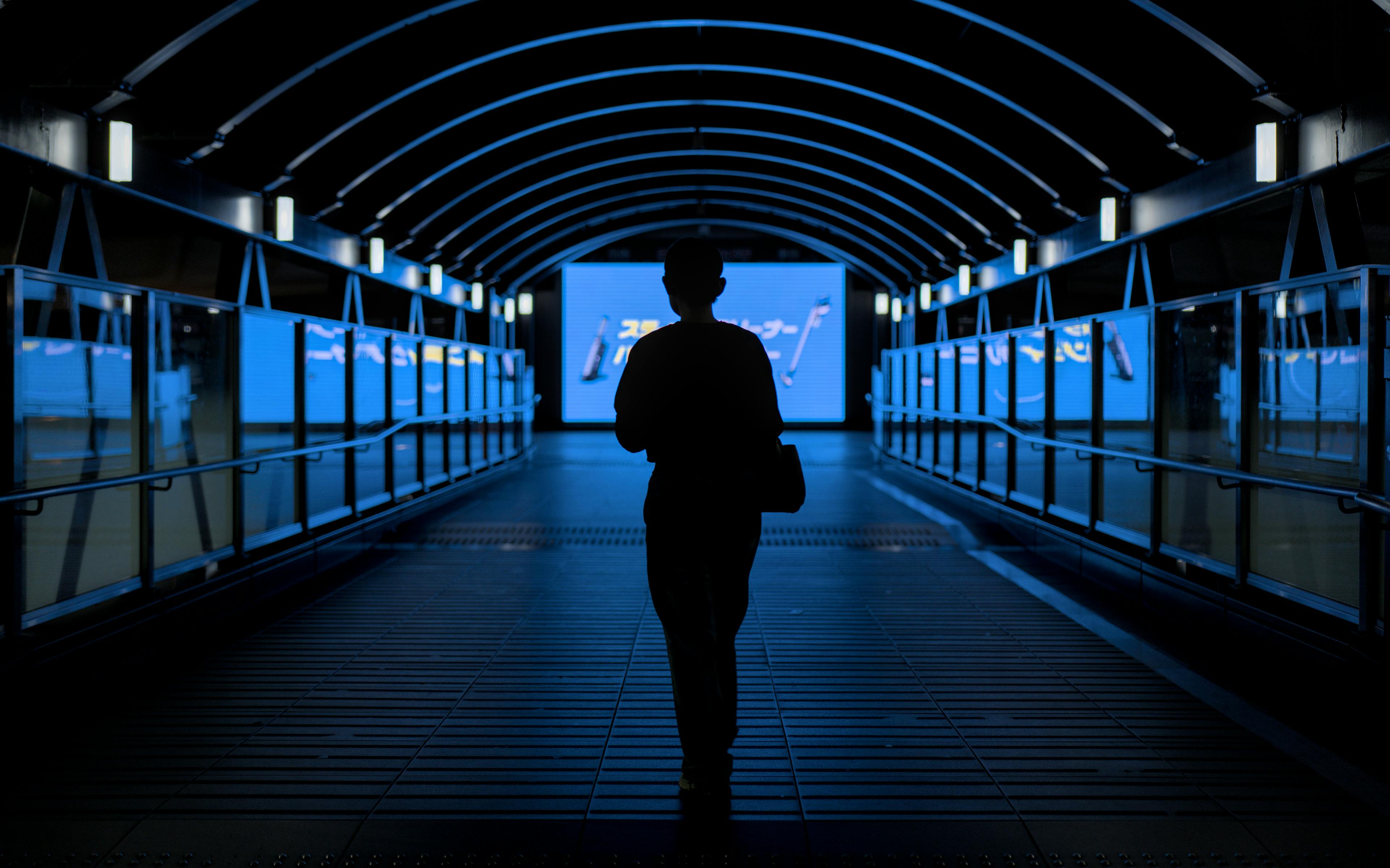 Mysterious silhouette walking through a blue-lit urban tunnel at night in Osaka, Japan.