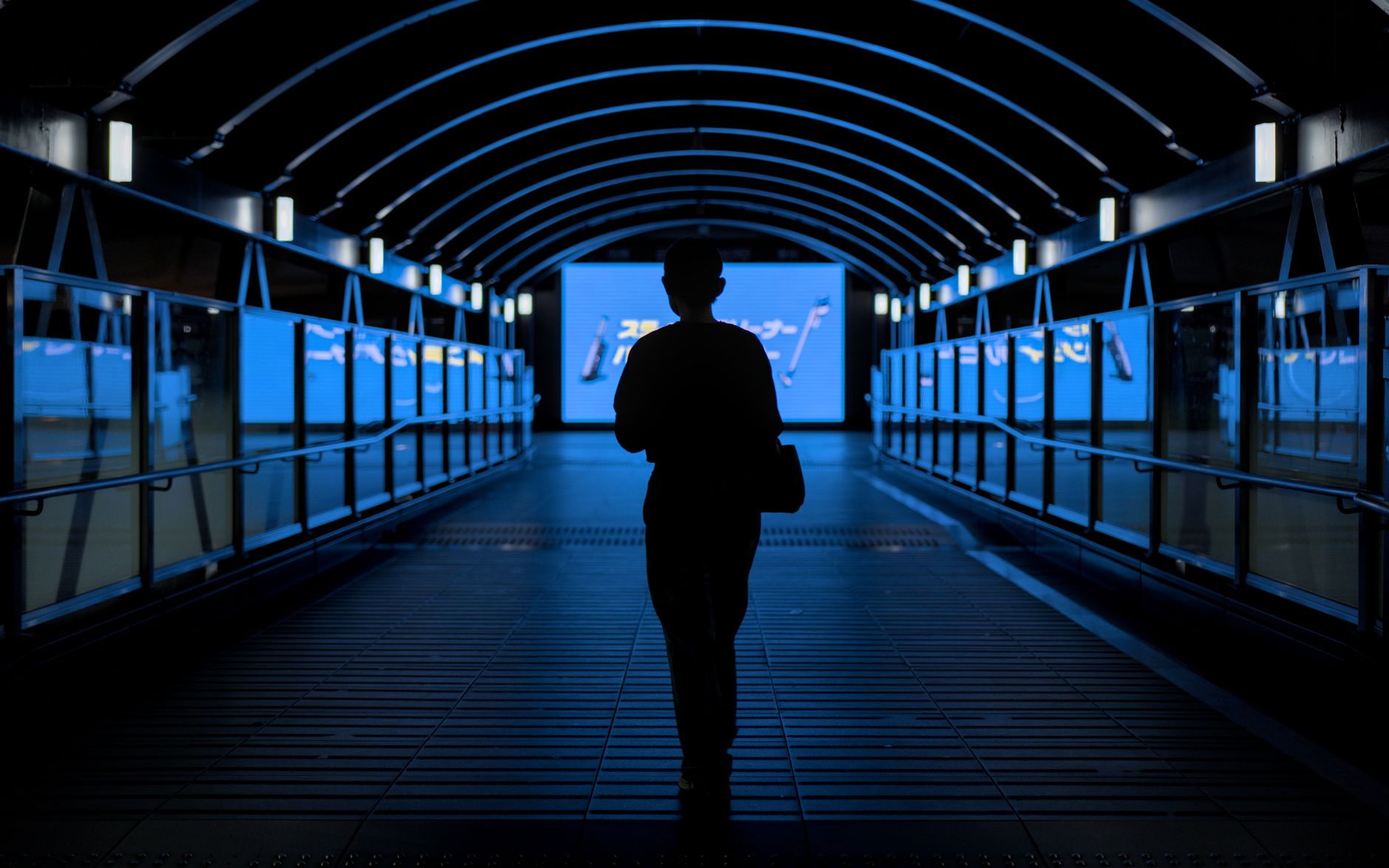Mysterious silhouette walking through a blue-lit urban tunnel at night in Osaka, Japan.
