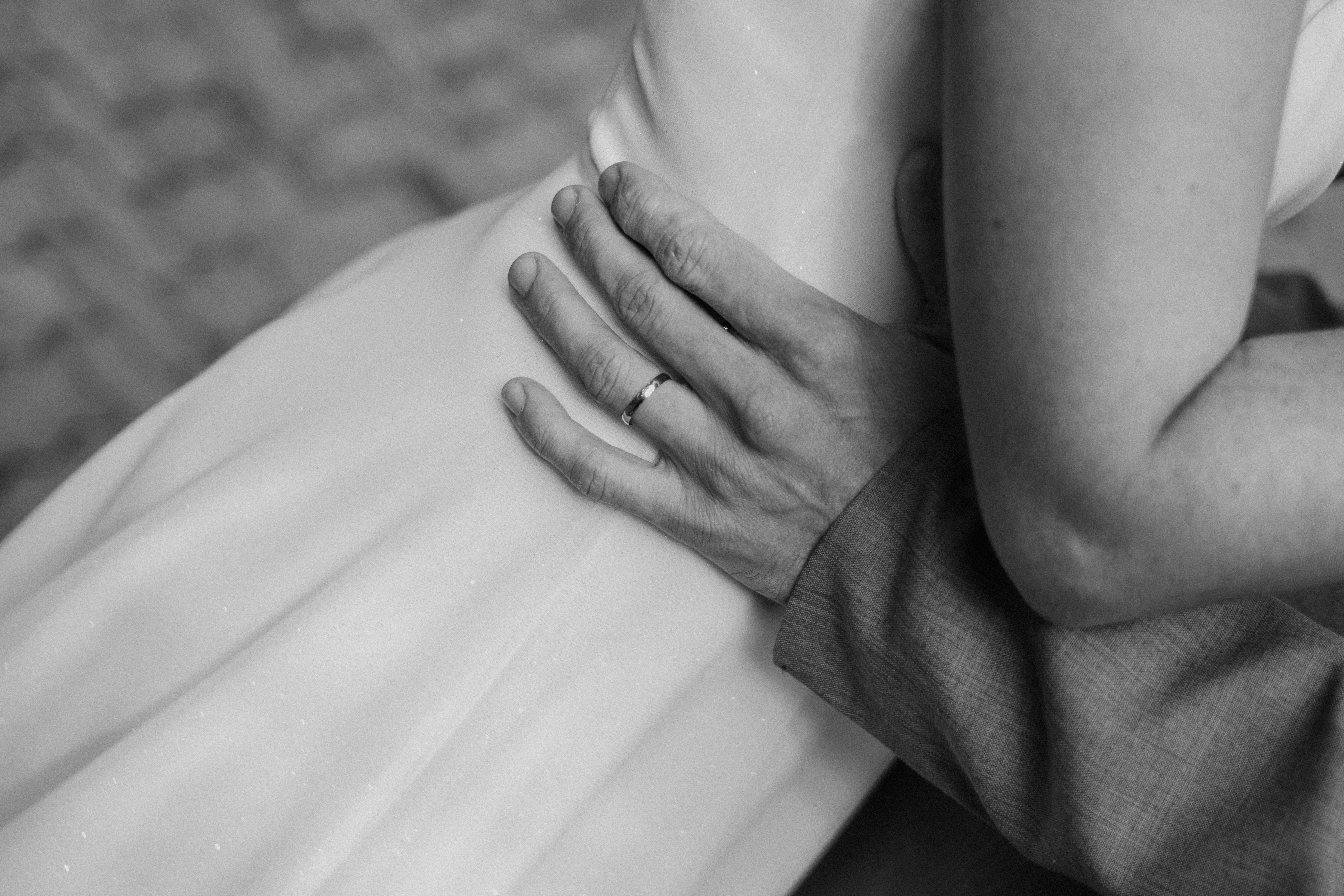 Closeup image of a couple embracing, highlighting a wedding ring in black and white.