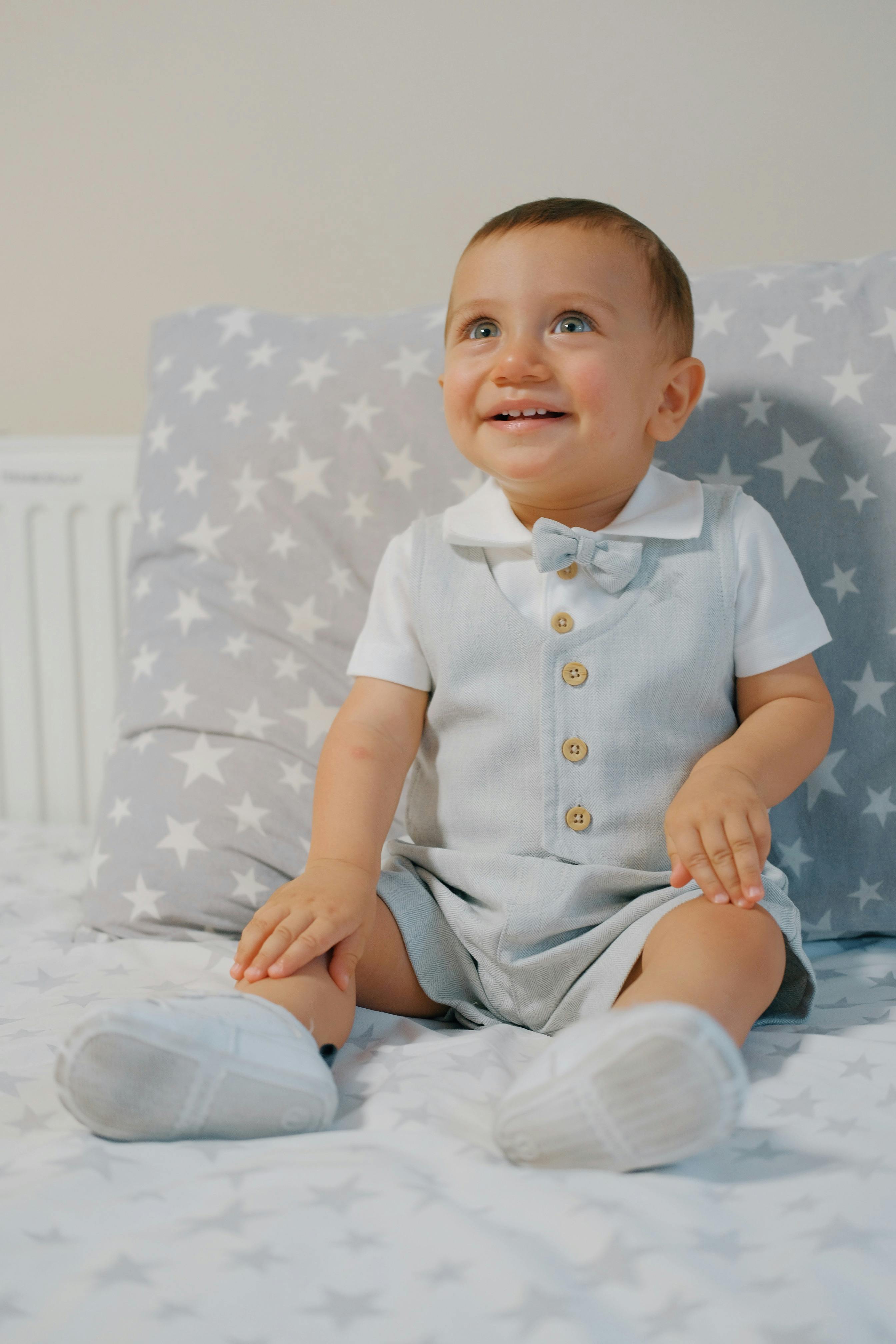 A cute baby in a smart outfit sitting happily on a bed with star-patterned bedding.