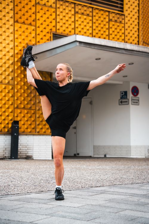Free Energetic dancer performing a high kick in front of geometric building in Berlin, Germany. Stock Photo