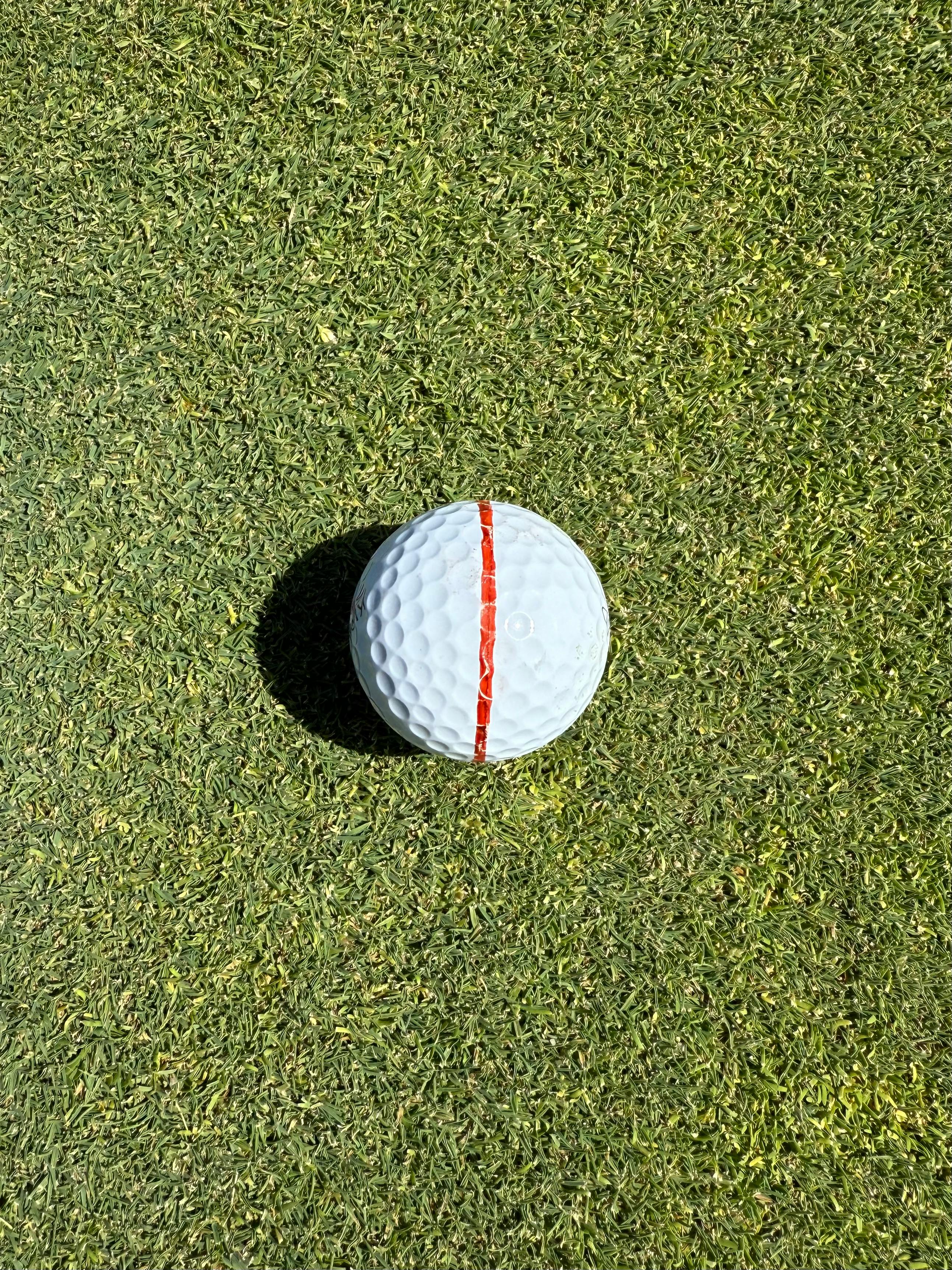 A golf ball aligned with a red stripe on a sunlit green, perfect for sports themes.