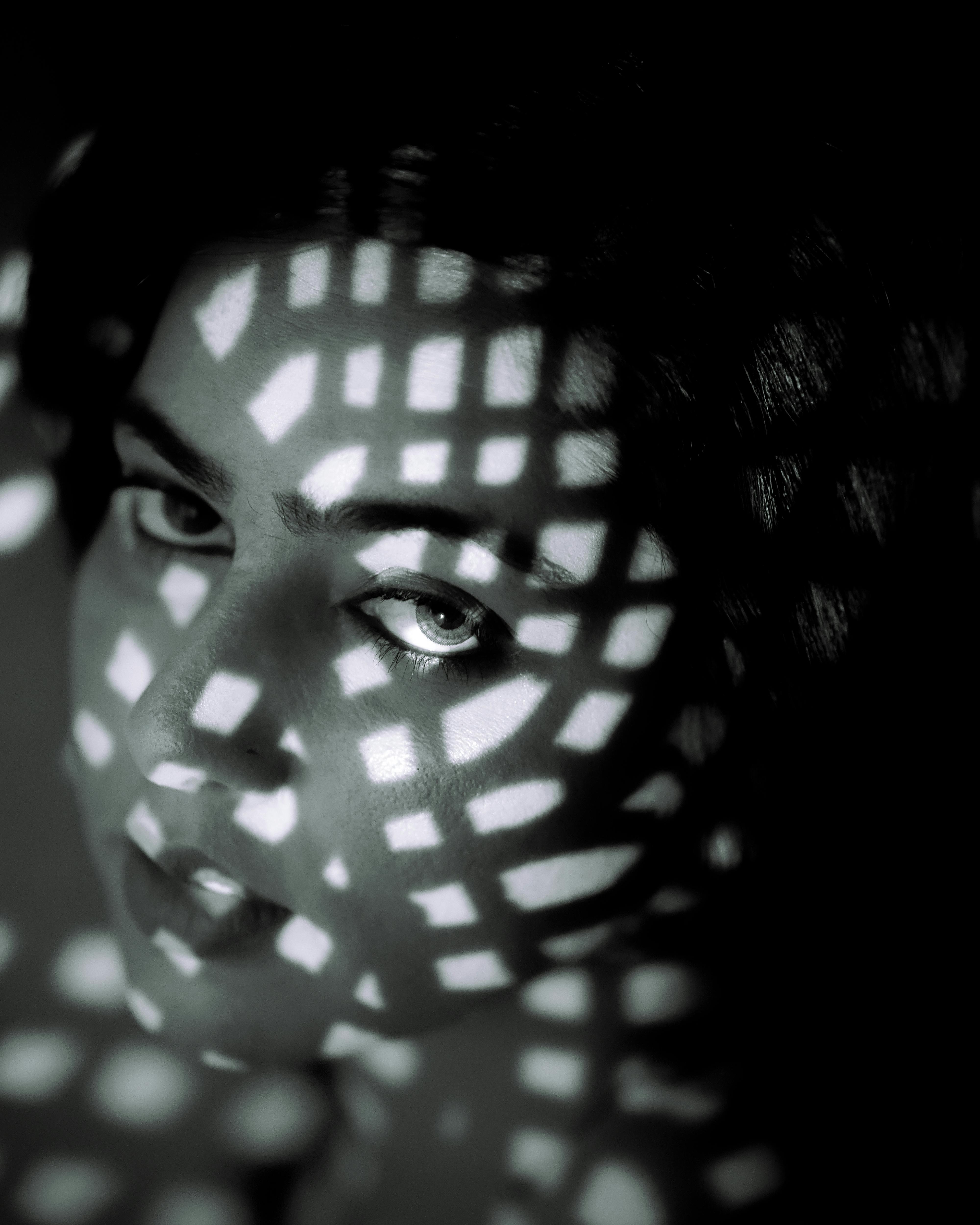 Dramatic portrait of a person in black and white with artistic light patterns creating a moody atmosphere.