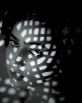 Dramatic portrait of a person in black and white with artistic light patterns creating a moody atmosphere.