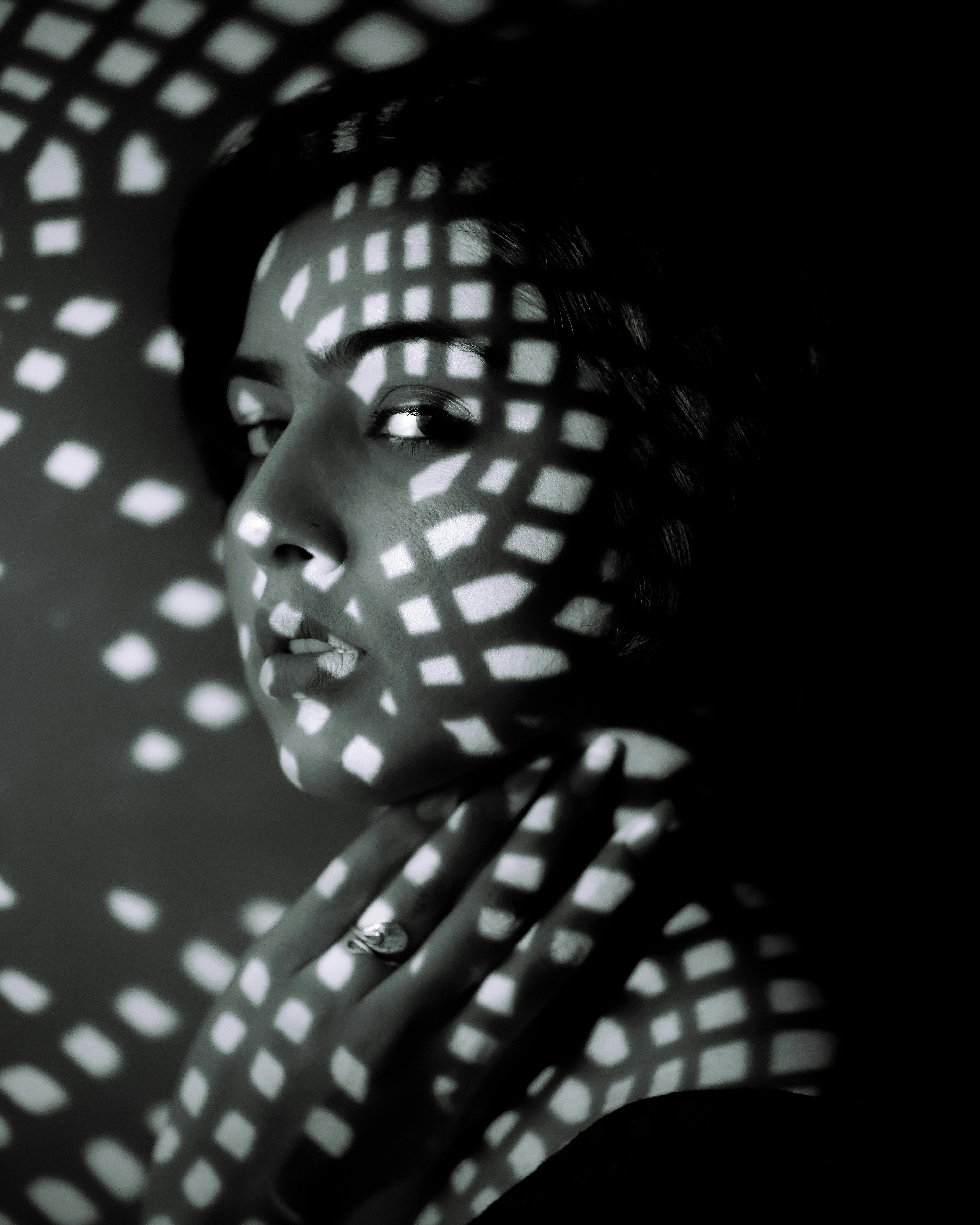 Black and white portrait with dramatic lattice lighting effect over a woman's face.