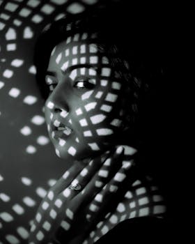 Black and white portrait with dramatic lattice lighting effect over a woman's face.