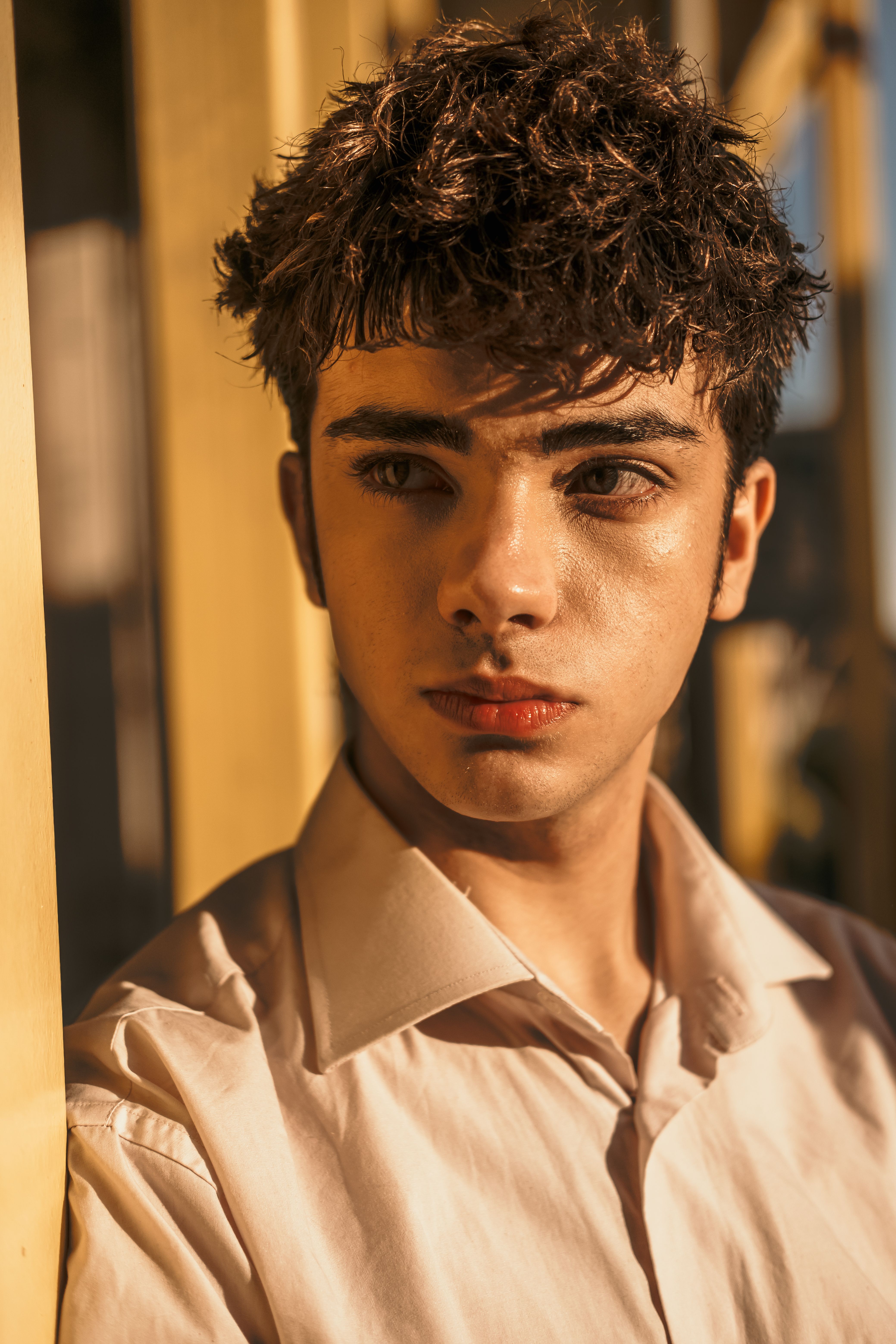 Close-up portrait of a young man with curly hair in a sunlit alley, İstanbul.