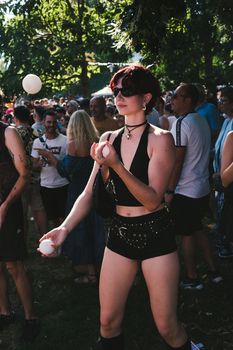 A vibrant outdoor festival scene with a woman juggling in the foreground, wearing sunglasses.