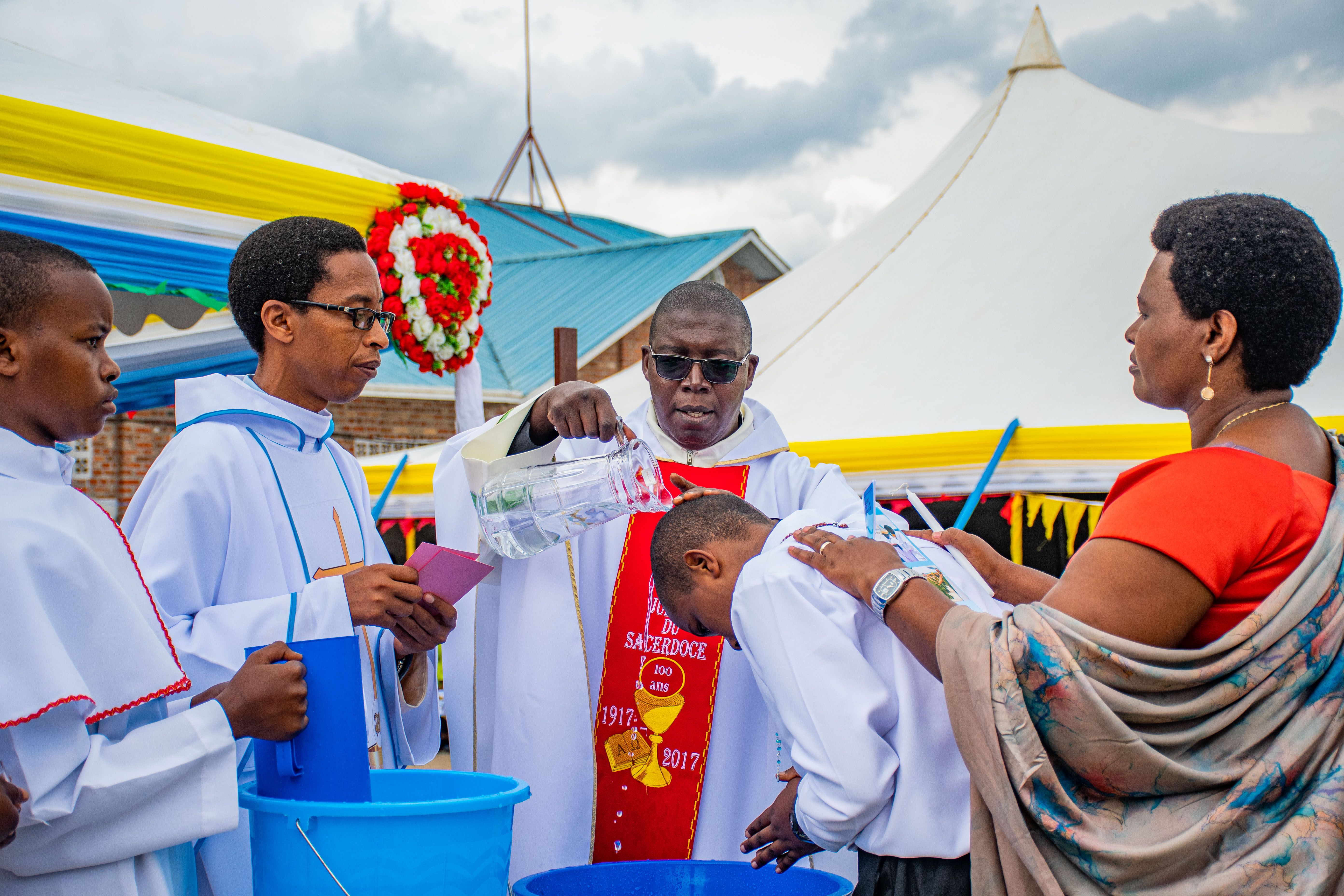 A vibrant outdoor baptism ceremony led by clergymen in white robes under tents.