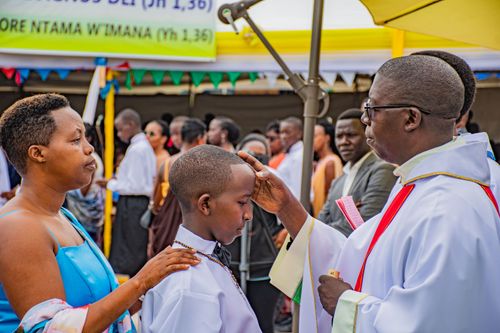 Free A boy receives a blessing during an outdoor religious ceremony with a priest, surrounded by family and guests. Stock Photo
