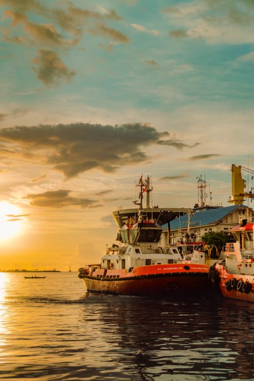 Free Colorful sunset at Makassar Harbor, South Sulawesi, with tugboats and a dramatic sky. Stock Photo