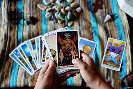 Hands holding tarot cards, focusing on 'El Diablo,' set on a colorful cloth background. Ideal for mysticism and fortune-telling themes.