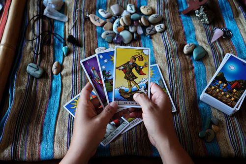 Free Close-up of hands holding tarot cards on a cloth, surrounded by runestones and crystals. Stock Photo
