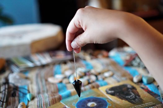Close-up of a hand holding a pendulum over tarot cards on a table.