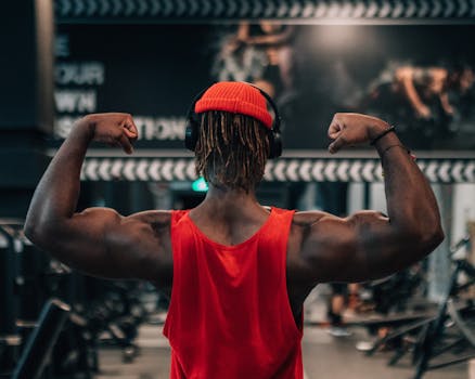 A man in a red tank top flexing his arm muscles in a gym setting, conveying motivation and strength.