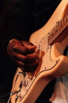 Close-up of a musician playing a white electric guitar, focusing on the guitar strings and hands.