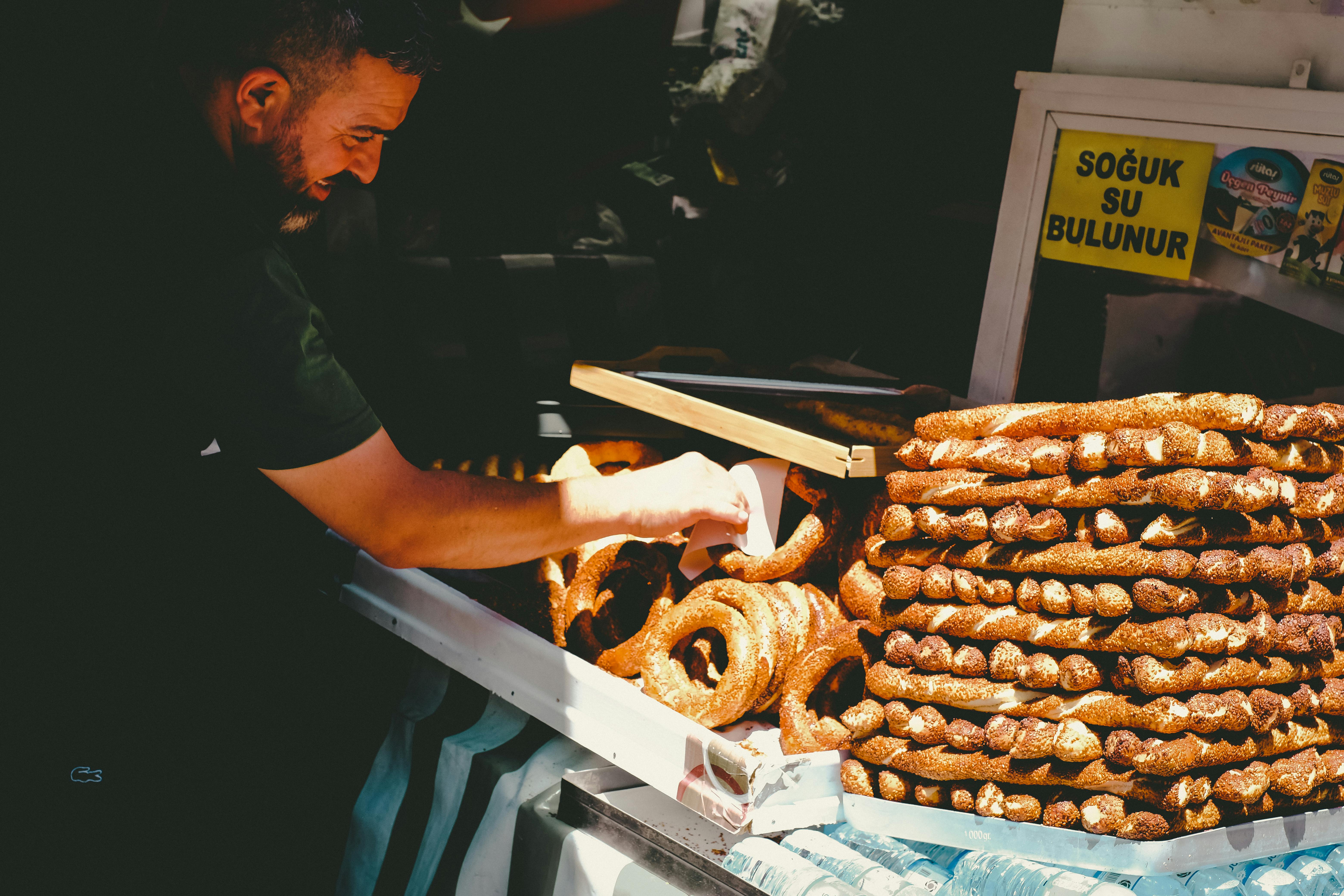 A vendor sells freshly baked traditional Turkish simit bread stacked in a street market setting
