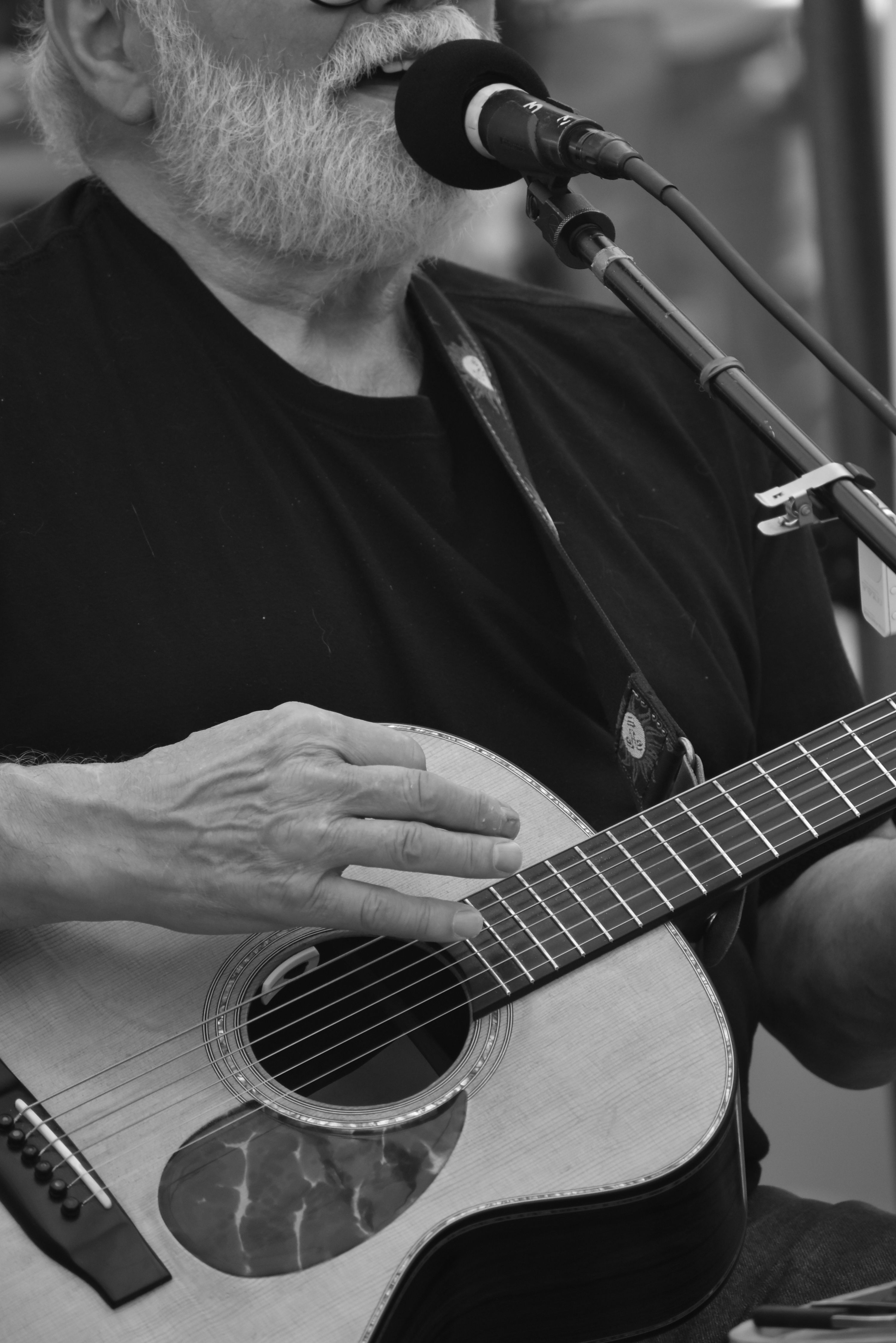 Black and white close-up of a musician strumming an acoustic guitar during a live performance.