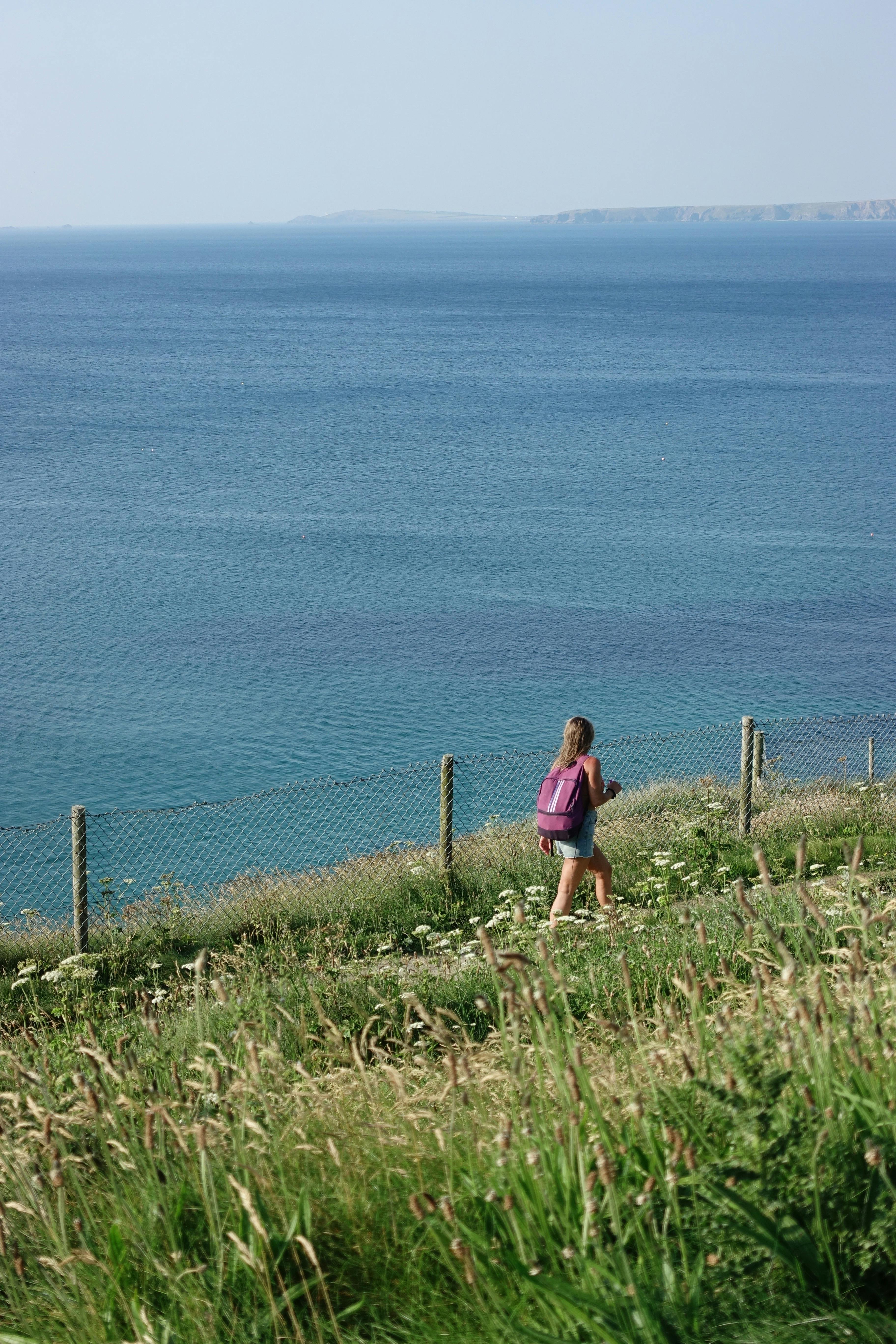 A young woman with a backpack hikes along a scenic cliff with a stunning ocean view.