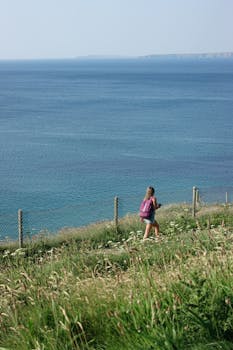 A young woman with a backpack hikes along a scenic cliff with a stunning ocean view.