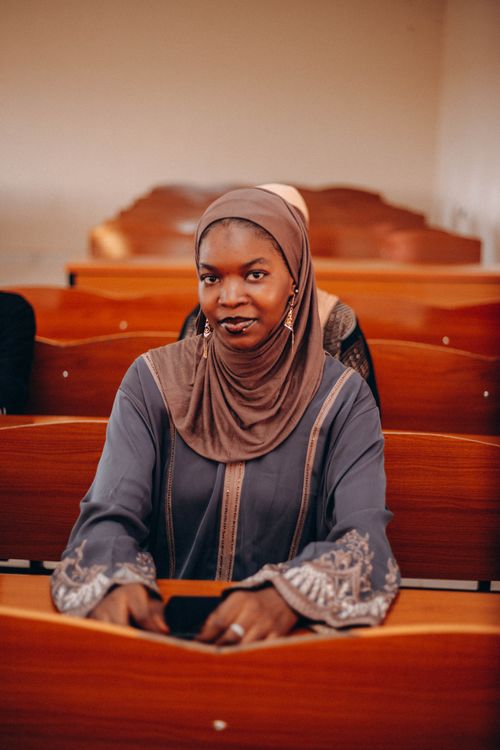Free Smiling woman in hijab sitting in a wooden classroom, exuding confidence and warmth. Stock Photo