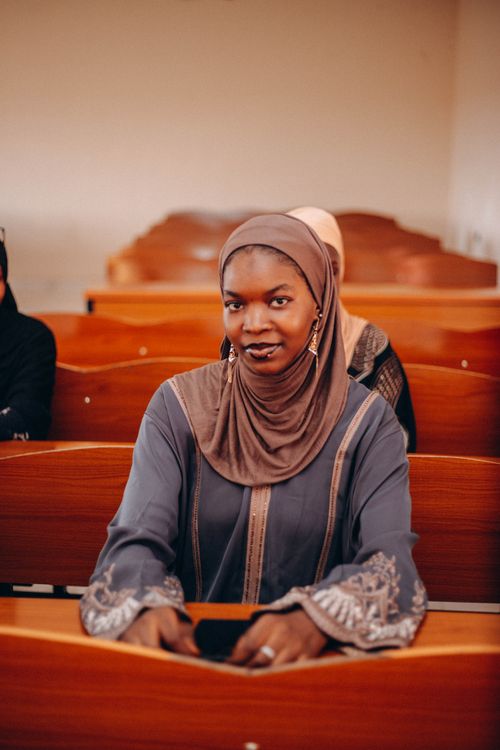 Free Smiling adult student wearing hijab sits in a classroom with wooden desks. Stock Photo
