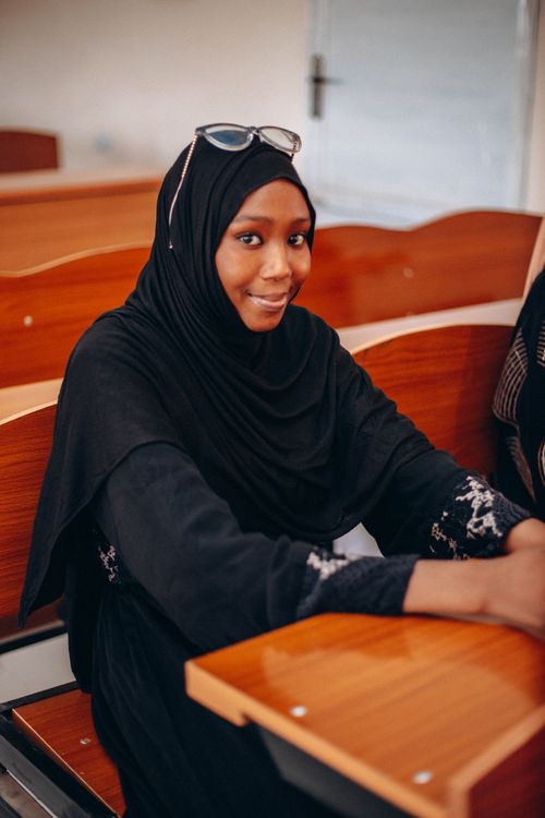 Free Smiling young woman wearing a hijab sitting in a classroom, exuding confidence and positivity. Stock Photo