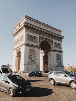 A bustling scene of the iconic Arc de Triomphe in Paris surrounded by city traffic under a clear sky.
