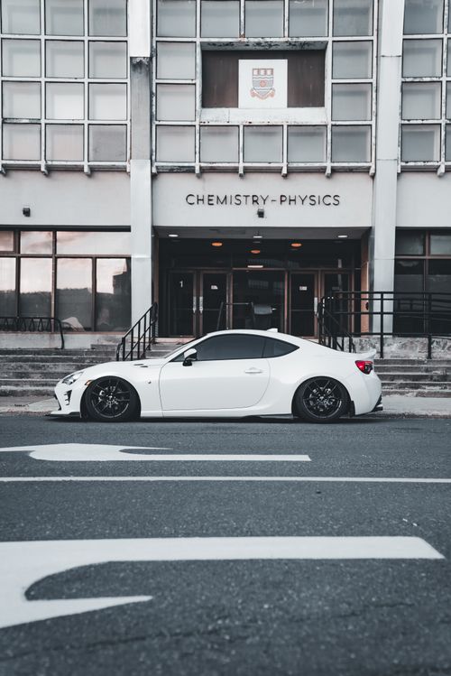 Free A sleek white sports car parked in front of a university's Chemistry-Physics building. Stock Photo