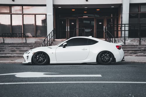 Free Stylish white sports coupe parked on a quiet city street outside a modern building. Stock Photo