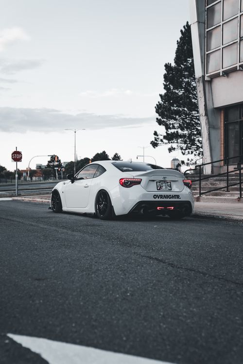 Free Sleek white sports car parked on city street in front of modern architecture. Stock Photo