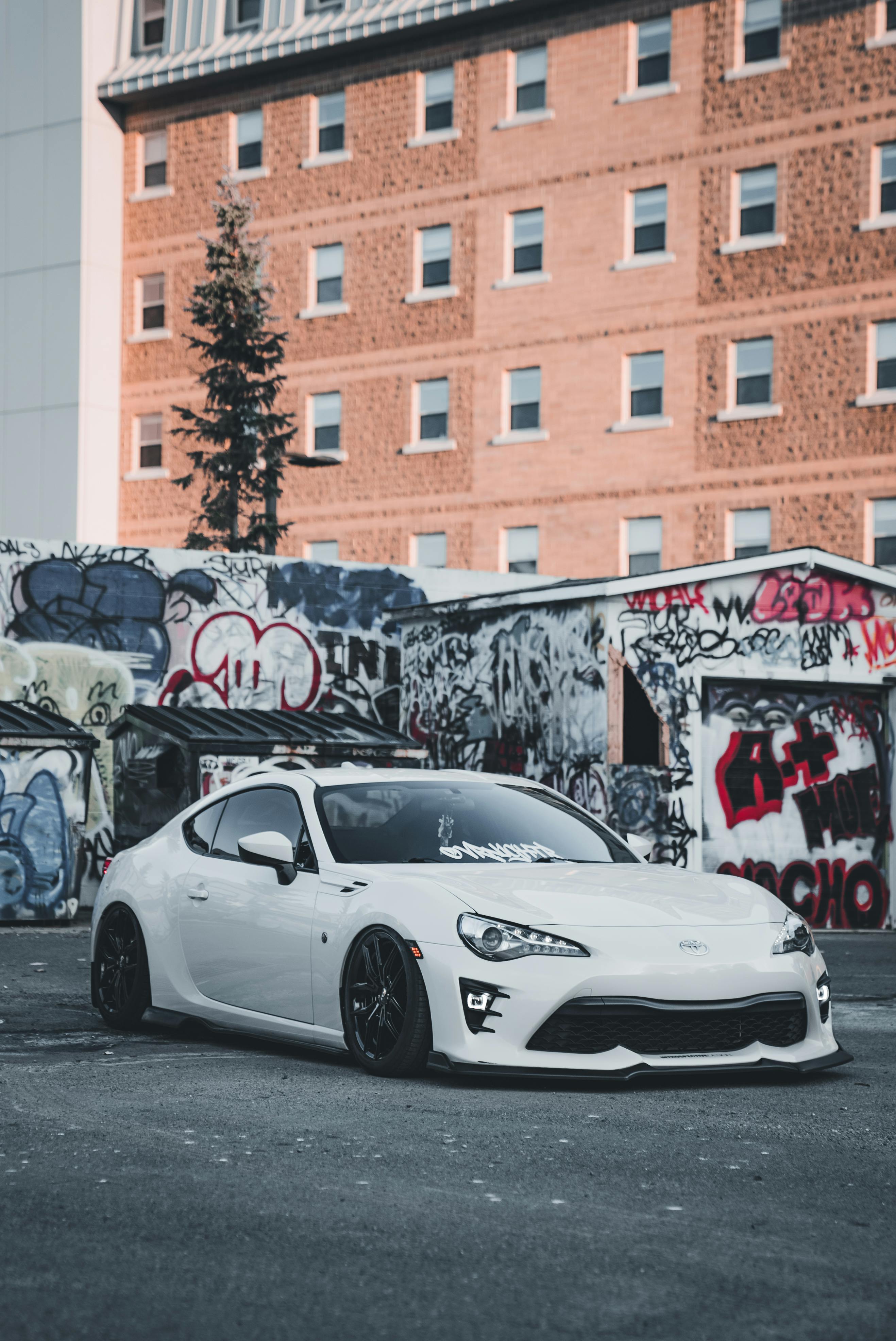 bezplatná Bílé sportovní auto zaparkované před zdmi pokrytými graffiti v městském prostředí. Základová fotografie